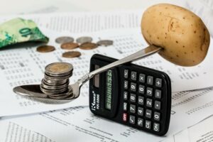 A spoon balanced on a calculator, with coins on the head and a potato jammed on the handle. Why? Budgeting.  Image from Pixabay by stevepb